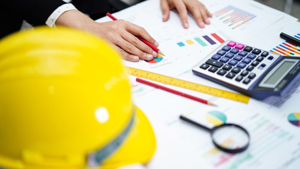Contractor reviewing financial charts with a calculator, hard hat, ruler, and pencil on the desk, symbolizing tax and business planning.