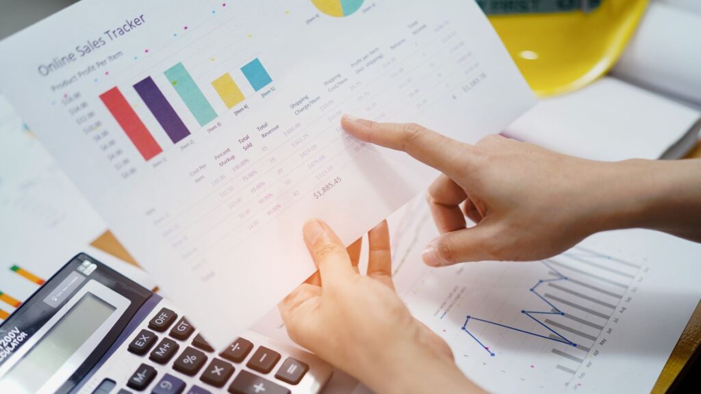 Hands pointing at sales and expense charts with a calculator and construction hard hat nearby, representing contractor tax planning.